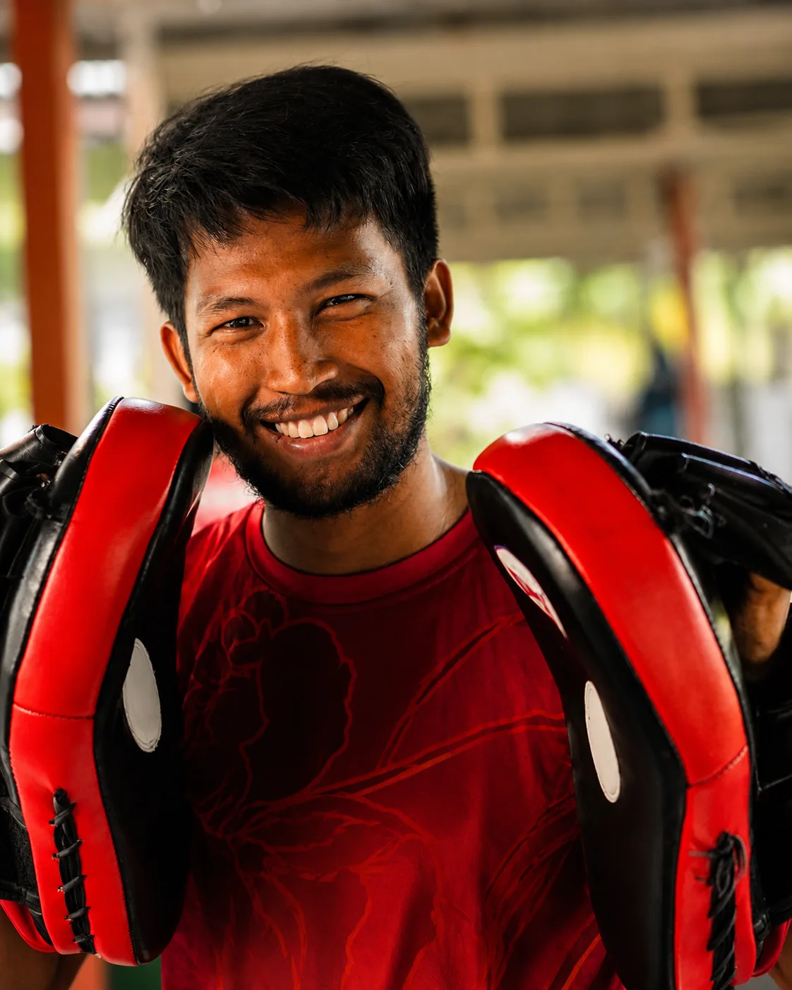 Muay Thai coach smiling with red focus pads at Phuket Cleanse