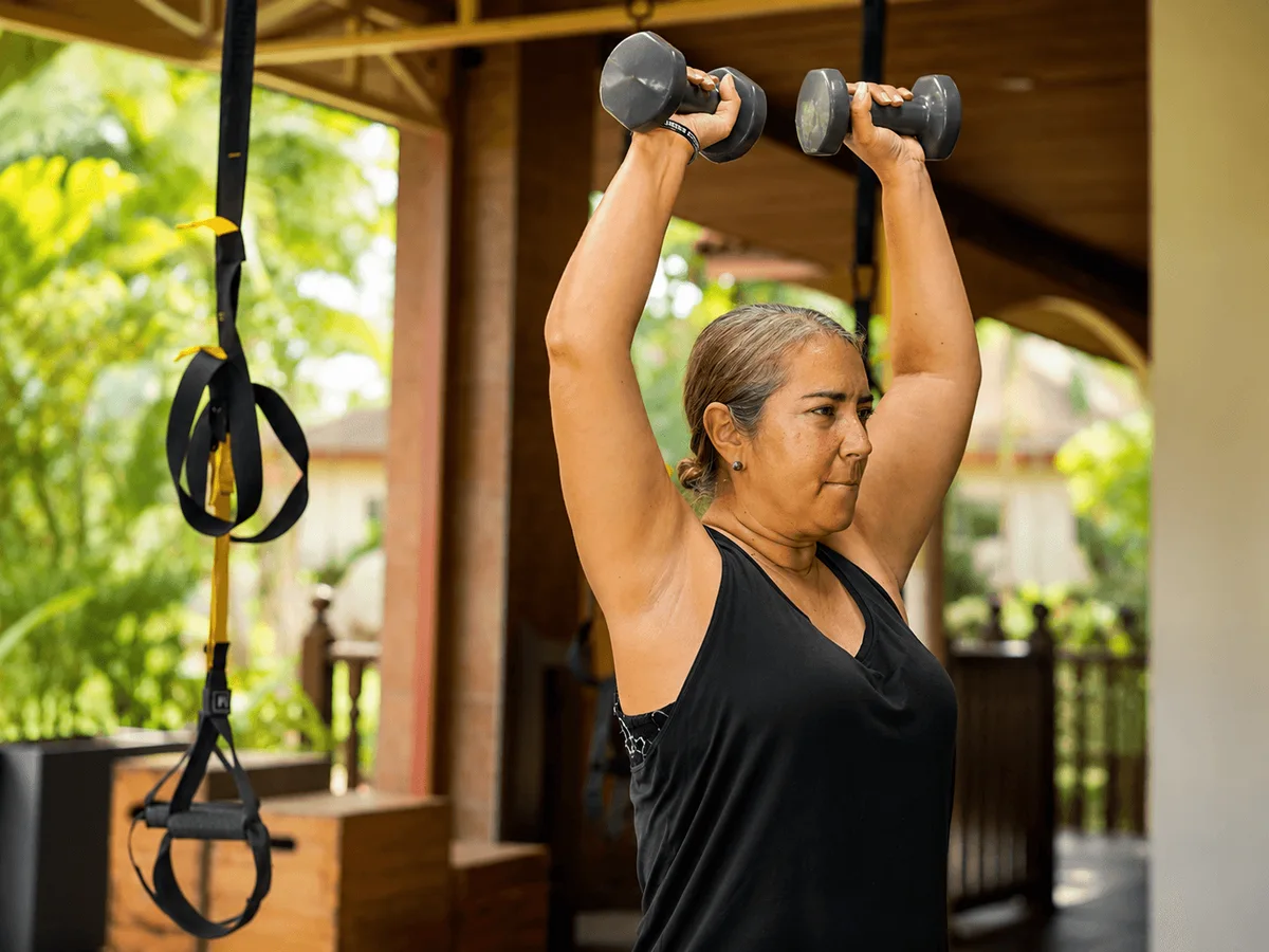 Woman doing dumbbell overhead press in the outdoor pavilion