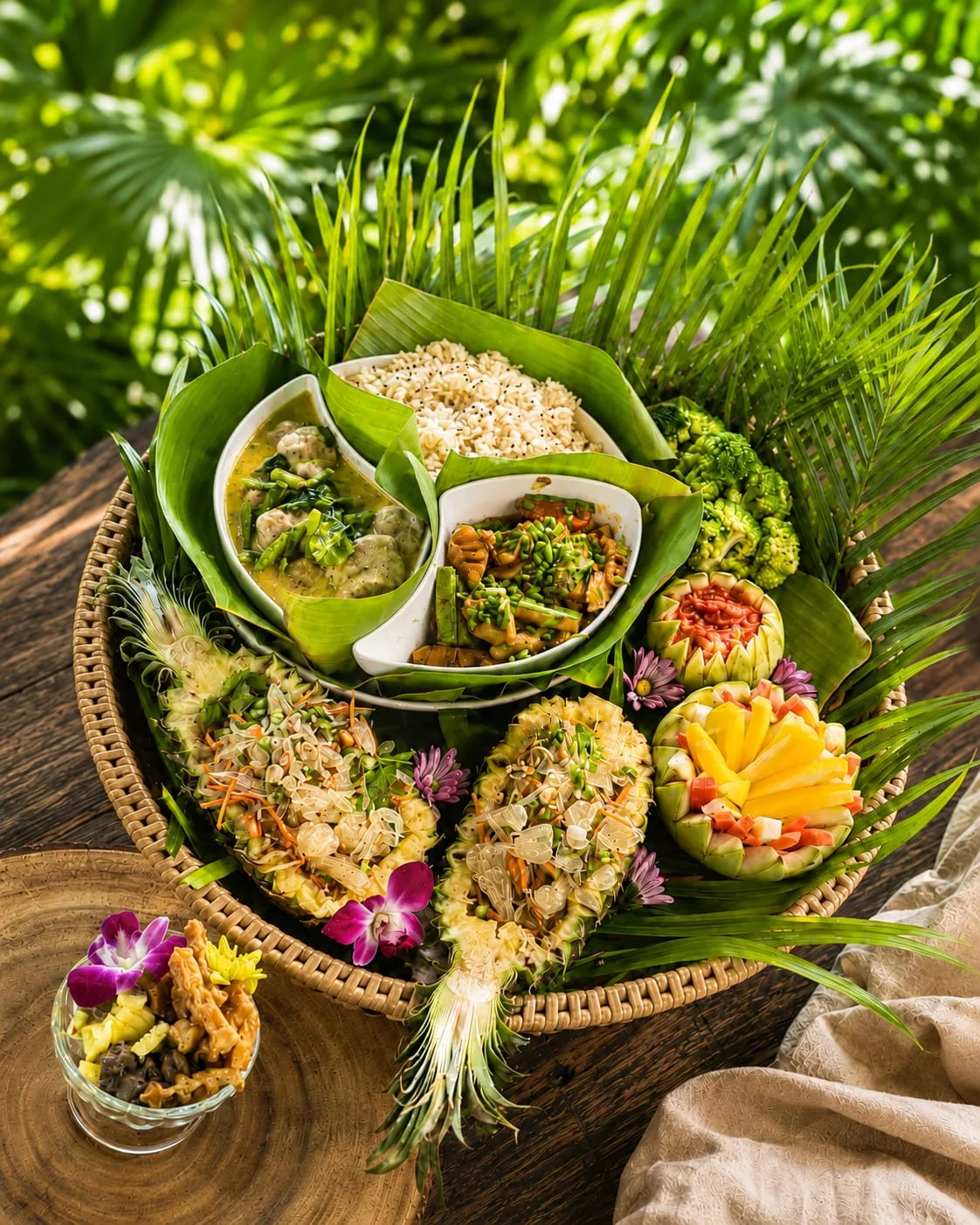 Elaborate Thai feast spread in a wicker basket with carved fruits, rice, curry and flowers
